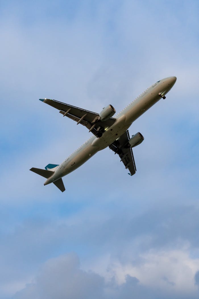 A commercial airplane soaring through a clear blue sky, viewed from below, showcasing its wings and engines.