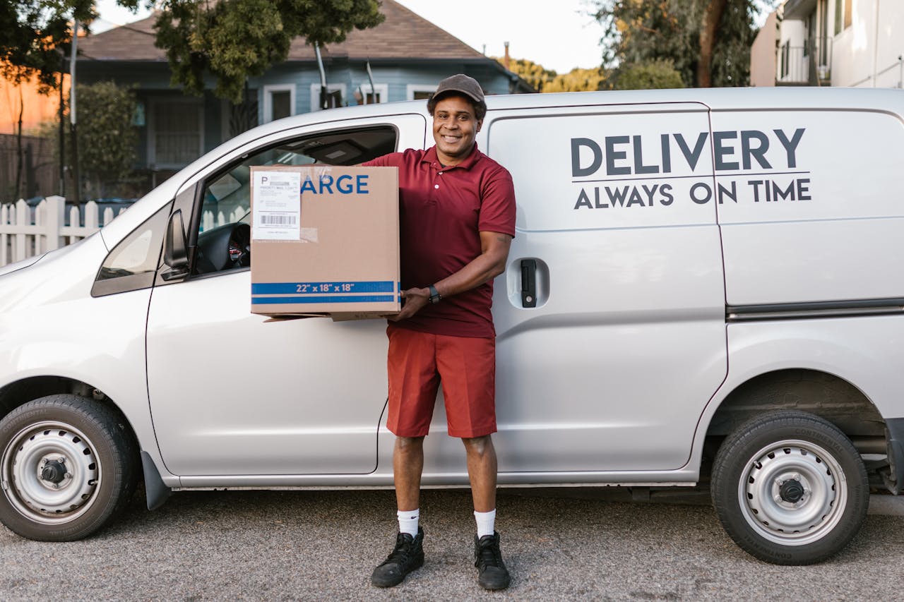 A courier in a maroon uniform smiling with a package in front of a delivery van.